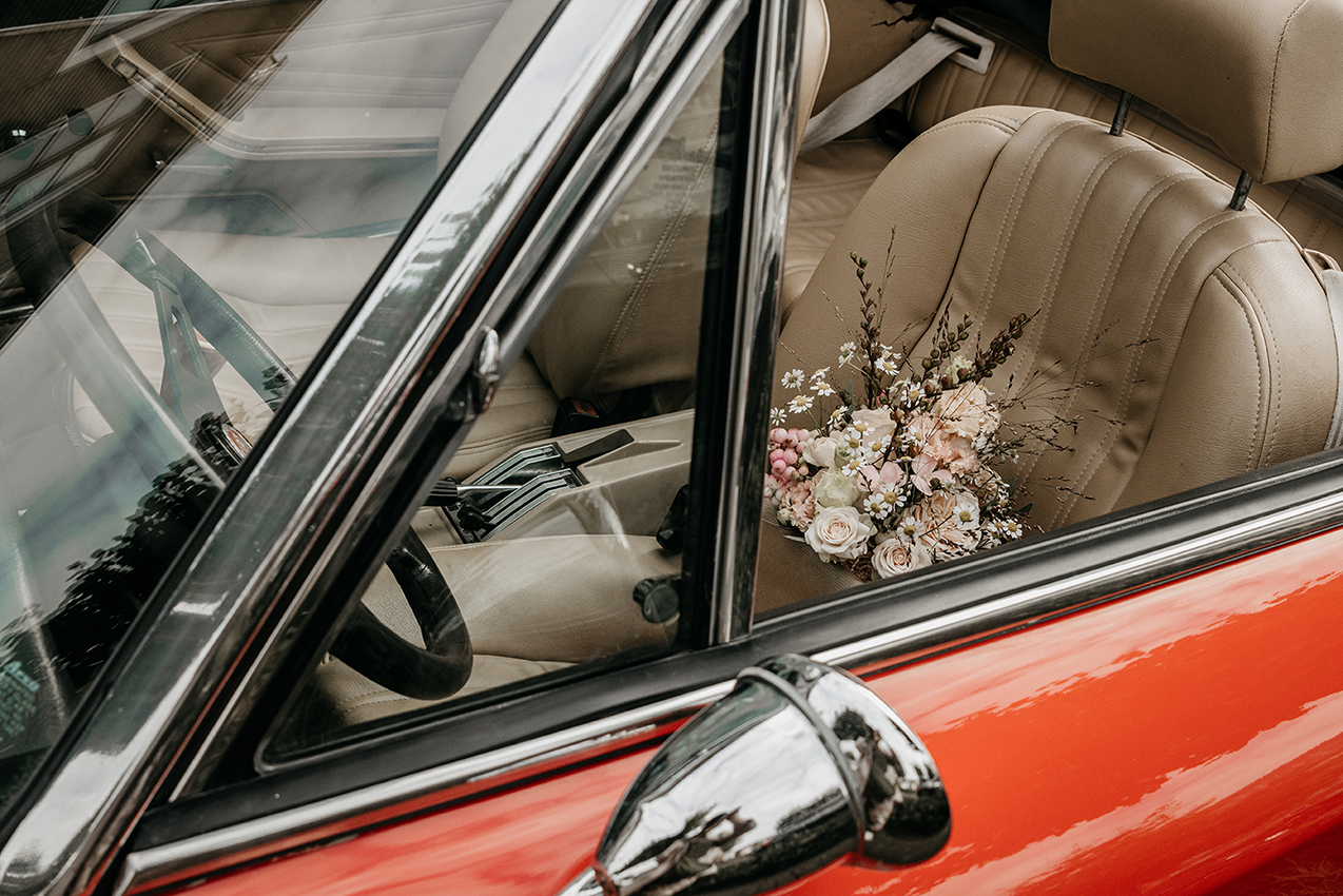 Foto van een rode oldtimer met een bruidsboeket, Goes.